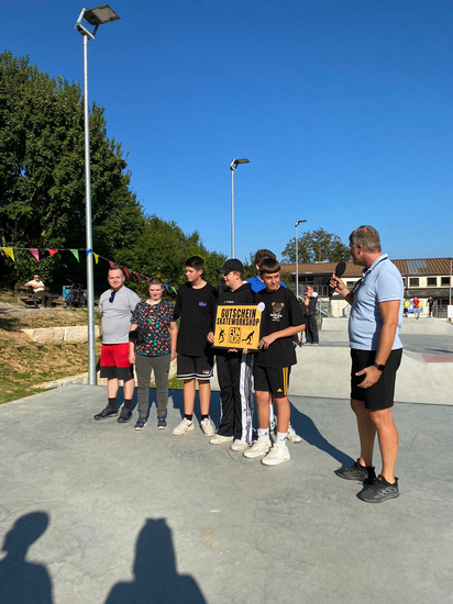 Menschen, die auf einer Skaterbahn stehen und einen Gutschein überreicht bekommen.