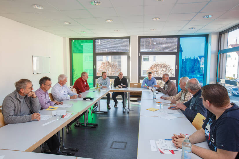 Menschen in einem Raum die an Tischen sitzen und diskutieren.