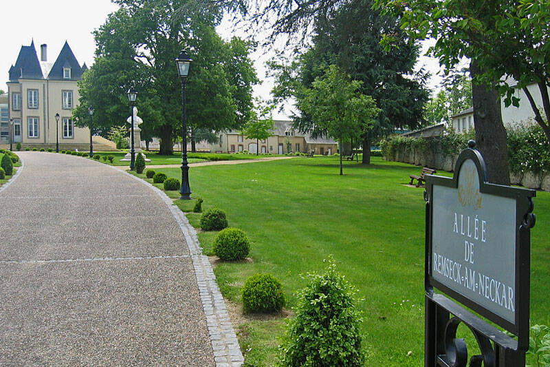 Park mit Bäumen und einem Kiesweg zu einem Gebäude im Hintergrund.