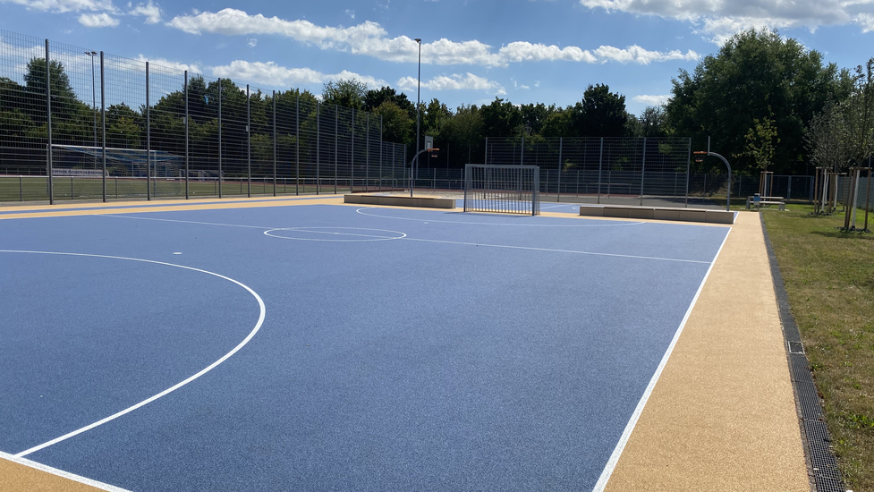 Sportanlage im Freien mit blauen Tartanboden. Tore und Basketballkörbe.