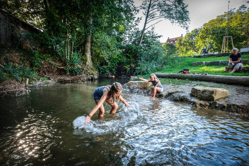 Zwei Kinder, die in einem Bach stehen und mit dem Wasser spielen.