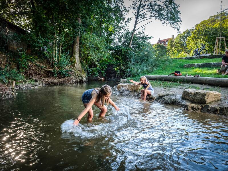 Zwei Kinder, die in einem Bach stehen und mit dem Wasser spielen.