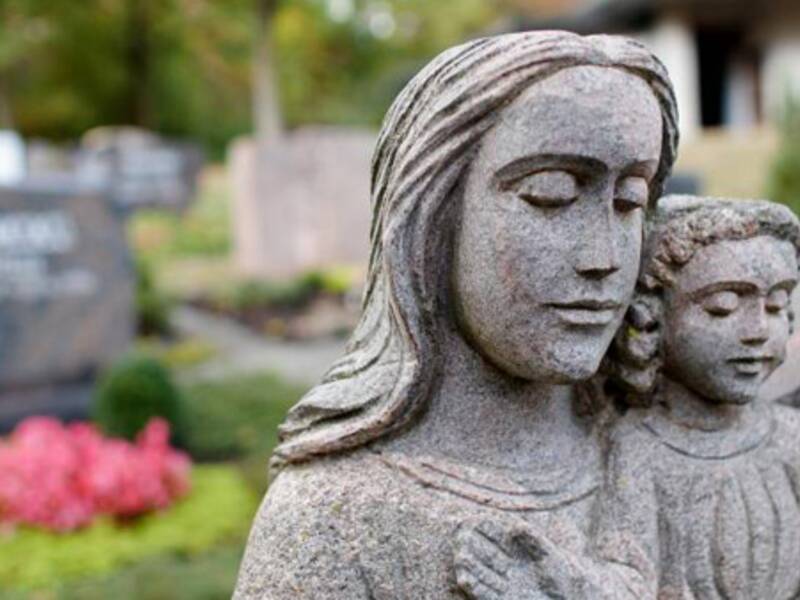 Steinstatue auf einem Friedhof, im Hintergrund Grabsteine.
