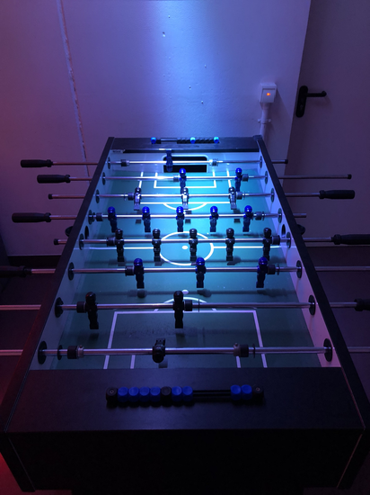 Tischkicker in einem dunklen Raum. Der Kicker wird nur mit einem kleinen Licht von oben beleuchtet.