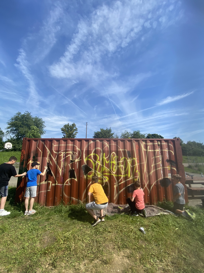Jugendliche, die einen Container mit Graffiti besprühen.