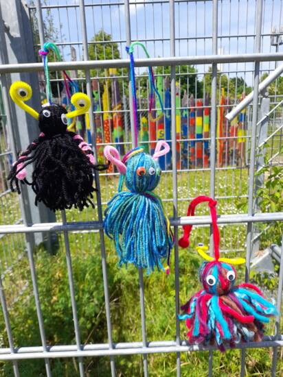 Selbstgebastelte Monster aus Wolle, die an einem Zaun hängen.