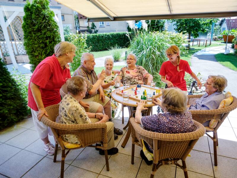 8 Menschen die auf einer Terrasse an einem Tisch sitzen und ein Spiel spielen.