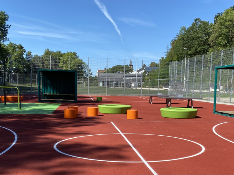 Rotes Tartanspielfeld mit Basketballkörben und Calestenics-Anlage.