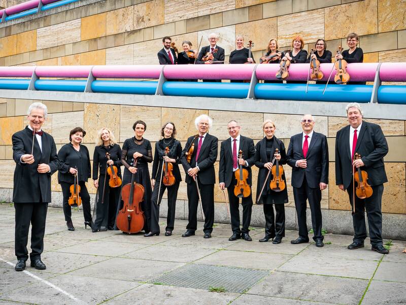 Orchester mit mehreren Musikern an einer Treppe. Alle sind schwarz gekleidet.